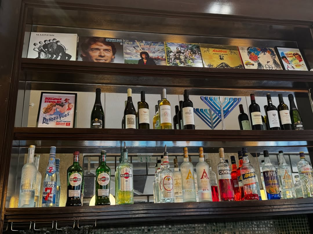 Étagères en bois du bar Rendez-Vous, avec bouteilles et pochettes de vinyles.